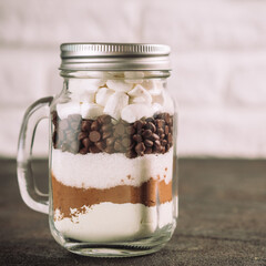 Hot chocolate mix in mason jar. Homemade mix from cocoa, dry milk, sugar, chocolate chips and marshmallows. Christmas and winter holiday budget-friendly holiday gifts idea. Copy space. Toned image