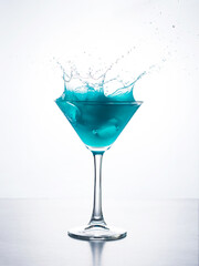 Blue cocktail in martini glass with ice cube splashing into liquid against white background. Blue curacao cocktail with splash on white.