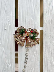 A decorative Christmas bell with golden glitter and red berries on white wooden fence. A decorative...
