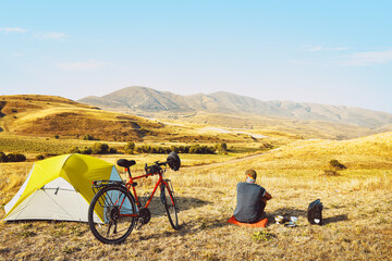 Adventurous cyclist sit by touring bicycle in mountains on side of green tent have break time rest...