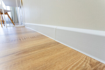 A detailed closeup photograph showcasing a modern wooden floor paired with a sleek white baseboard...