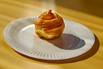 An éclair dessert on a white plate in sunlight against a yellow background, portioned dessert presentation