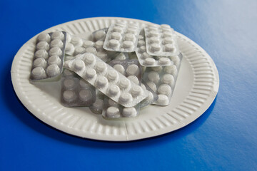 Blisters with white tablets on a white paper plate on an overall blue background, close-up, daily...