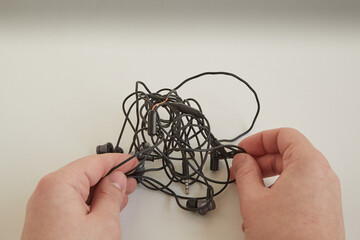 Two hands untangling tangled wires from phone headphones, tangled wires in hands, tangled wires, closeup