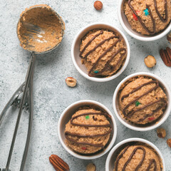 Safe-to-eat raw monster cookie dough in small portion bowl, ice cream scoop and nuts on gray cement background. Ideas and recipes for kids and toddlers meal. Top view or flat-lay