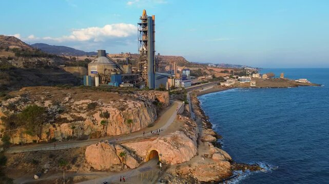 Drone flight along the beach Penon del Cuervo of Malaga overlooking a big rock in the sea, the cement factory and mountains in the background. 