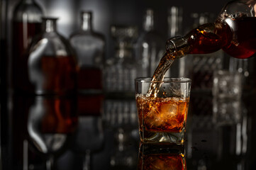 Whiskey is poured from a bottle into a glass with ice.