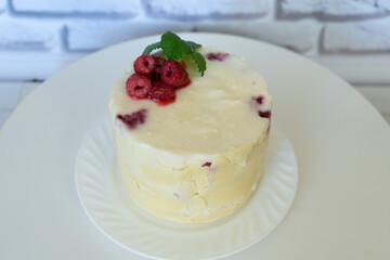 Homemade cake covered with white chocolate and decorated with red spring raspberry, green mint leaf Imperfect baking, pastry at home Colorful cake and fresh berries on white plate
