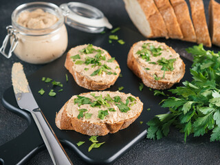 Close up view of slice bread with homemade turkey pate and fresh green parsley on black kutting board over black cement background,