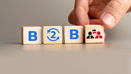 B2B Concept with Wooden Cubes Displaying Business to Business Collaboration, Hand Arranging Cubes with Arrows and People Icons, Symbolizing Partnerships and Exchanges.