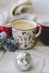 A warm beverage sits in a decorative mug next to a gift and holiday ornaments, creating a cozy atmosphere perfect for winter relaxation.