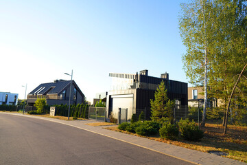 Obraz premium Modern luxury Villa. Street Road in Contemporary Residence with Barnhouse. Modern Barn house. Barn home with lawn, shrubs, green courtyard in sustainable enviroment. Family House in Gated Community.