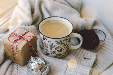 A warm beverage sits in a decorative mug next to a gift and holiday ornaments, creating a cozy atmosphere perfect for winter relaxation.