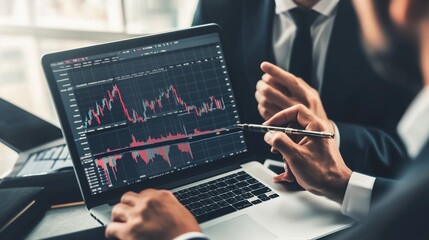 Business professionals analyzing stock market trends on a laptop during a meeting in a modern office environment
