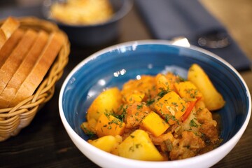 yellow food in a blue plate. vegetable stew with potatoes carrots pepper sprinkled with herbs. High quality photo food on a wooden table. The view of the food is shot at 45 degrees. There is also