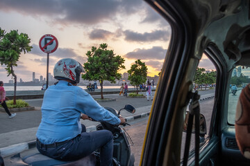 A man rides a scooter down the bay in the City as seen from the back of a car
