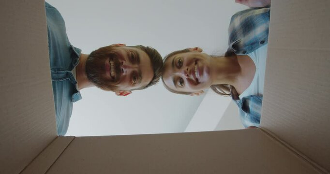 Young happy couple opening cardboard box after relocation and looking inside kissing in new house.