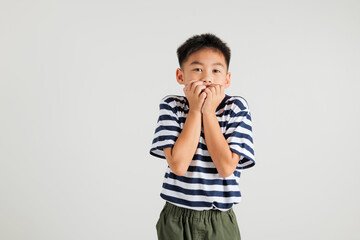 Asian portrait cute young kid boy standing amazed, shocked afraid mouth covered gesturing hand palms looking camera, studio shot isolated on white background, Thai primary child scared