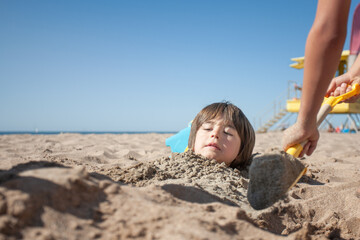 Boy with a worried face when he sees himself buried under the sand on the beach.