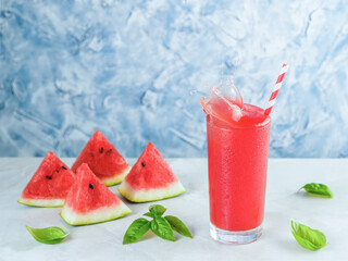 Tasty appetizing watermelon drink with basil in in glass on gray table. Homemade watermelon and basil lemonade with splashes. Copy space. Slice watermelon and green basil leaves on background