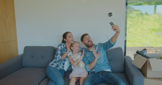 Beautiful family making memorable selfies on smartphone while relaxing, sitting between cardboard boxes after house move.