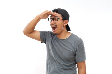 Naklejka premium Asian man wearing casual t-shirt and glasses standing over white background very happy and smiling looking far away with hand over head. Searching concept.