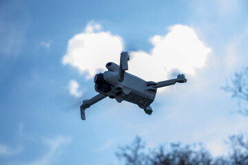 A flying drone captured against a blue sky with clouds, in an outdoor setting. The drone's details are clearly visible, featuring its modern design and technology in action.