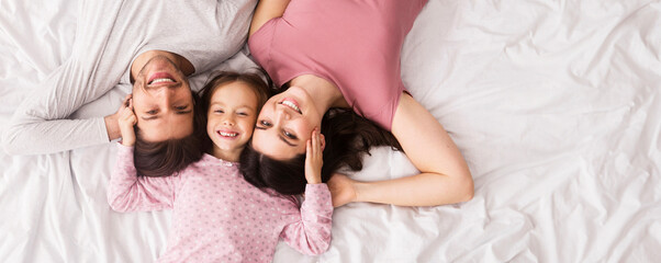 Family Love. Portrait Of Affectionate Parents And Their Little Daughter Lying Tohether In Bed And Embracing, Top View