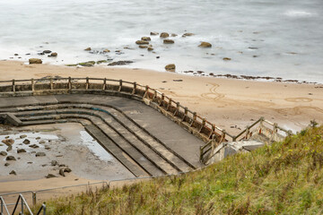 Derelict forlorn ruin of outdoor swimming pool at sea water ocean of bygone glory days of long ago near Newcastle, England, UK