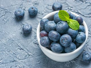 Freshly picked blueberries closeup. Ripe and juicy fresh blueberry with green mint leaves on textured concrete background. Bilberry on gray background with copyspace. Top view or flat lay
