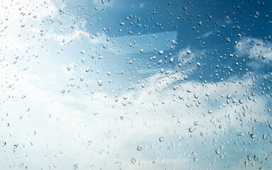 Beautiful raindrops on wet glass with a bright blue sky and scattered clouds in the background....