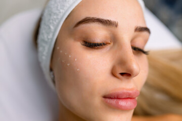 Beautiful relaxed woman at beautician cabinet receiving anti wrinkle injections on cheekbones, lying with closed eyes in beauty salon