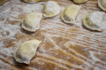 Traditional homemade Polish pierogi dumplings on a wooden surface dusted with flour, ready to cook. Handcrafted, unleavened dough, popular Eastern European dish.