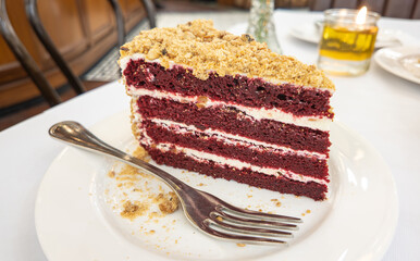 Red velvet cake with chopped peanuts topping served on white ceramic plate with fork. Concept for sweet food and dessert.