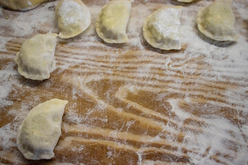 Handmade traditional Polish dumplings, pierogi, placed on a wooden surface dusted with flour, ready to be cooked. A rustic and homely representation of Eastern European cuisine.