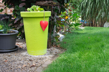 Bright green garden pot with red heart ornament on gravel surface