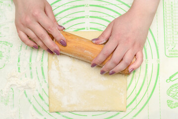 Hands rolling dough with a rolling pin on a green baking mat.