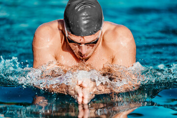 Swimming man. Male swimmer swimming breaststroke. Portrait of man doing breast stroke swimming in pool outside wearing red swimming cap and swim goggles. Fit athlete training.