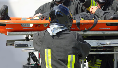 firefighter wearing a uniform and helmet carries a injured person on a stretcher