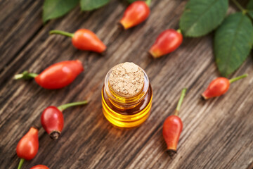 A glass bottle of rose hip seed oil with fresh rosehips on a table