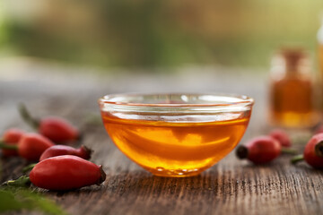 A bowl of rose hip seed oil with fresh rosehips on a table