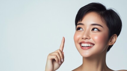A smiling Asian woman points to the side against a clean white background, showcasing her natural beauty and genuine expression. 