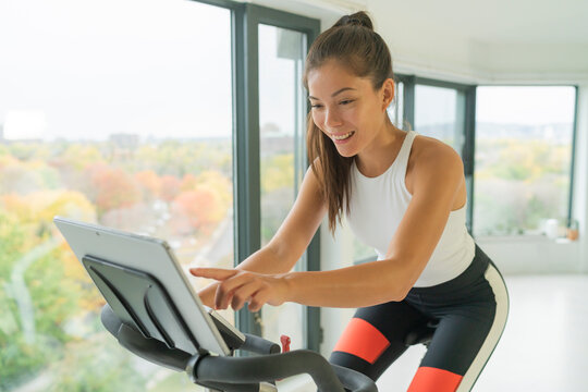 Indoor training bike. Exercise at home indoor cycling with online class on screen. Woman training cardio biking on workout spin bike active fitness lifestyle.