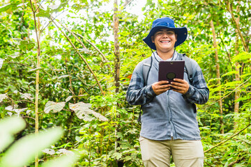A biologist in field clothing smiles at the camera while holding a tablet, using it for his...