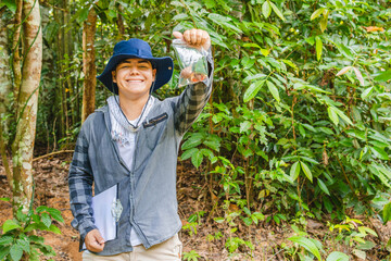 A biologist smiles at the camera while holding a seed sample from a plant he was researching