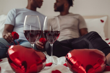 Happy homosexual male couple celebrating love and valentine's day with wine, heart shaped balloons and chocolate. High quality photo