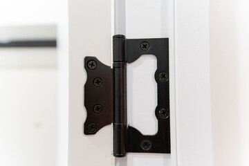 This image showcases a detailed closeup view of a black door hinge that is affixed to a white door, highlighting the contrast between the colors and materials used in this fixture