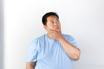 Thoughtful Asian man wearing blue t-shirt holding his chin and thinking with serious expression consider something.