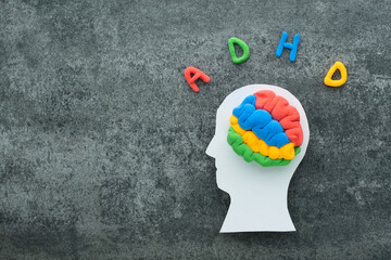 A brain model crafted from colorful materials rests on a white head silhouette, with the letters ADHD on a concrete background. ADHD and learning difficulties awareness and support