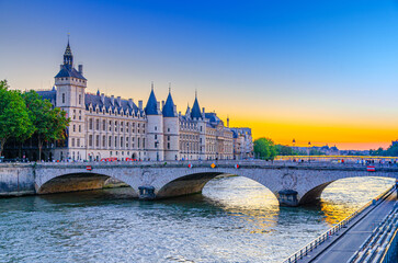 Naklejka premium Paris city historic center with Pont au Change bridge across Seine river, Conciergerie palace Gothic revival architecture style on Île de la Cite island on sunset twilight, Paris evening view, France